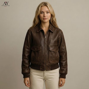 May include: A brown leather bomber jacket with a zip-up front, two front pockets, and a ribbed hem and cuffs. The jacket has a classic collar and a vintage, distressed look. The logo "AY COLLECTION" is in the top left corner.