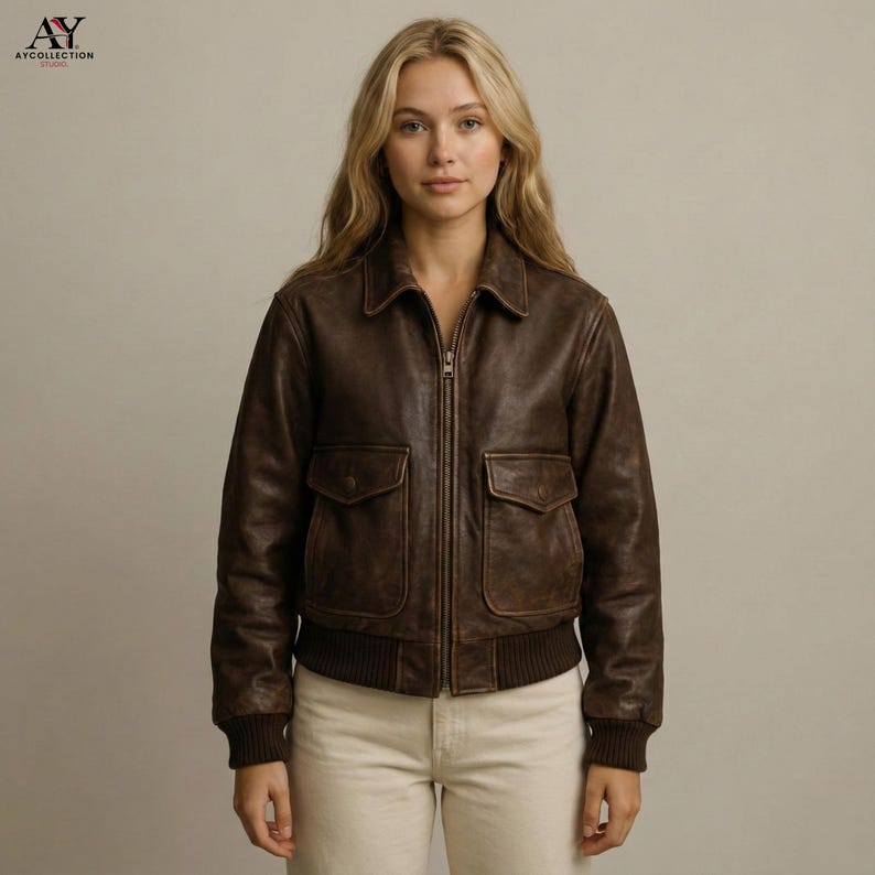 May include: A brown leather bomber jacket with a zip-up front, two front pockets, and a ribbed hem and cuffs. The jacket has a classic collar and a vintage, distressed look. The logo "AY COLLECTION" is in the top left corner.