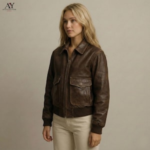 May include: A brown leather jacket with a zip-up front, two front pockets, and a collared neckline. The jacket has a ribbed hem and cuffs. The logo "AY COLLECTION" is in the top left corner.