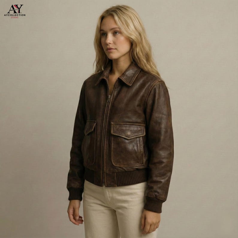 May include: A brown leather jacket with a zip-up front, two front pockets, and a collared neckline. The jacket has a ribbed hem and cuffs. The logo "AY COLLECTION" is in the top left corner.