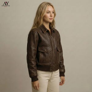 May include: A brown leather bomber jacket with a zip-up front, two front pockets, and a ribbed hem and cuffs. The jacket has a classic collar and a vintage look. The model is wearing the jacket with light-colored pants.
