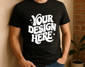 May include: Black crew neck t-shirt with the text "YOUR DESIGN HERE" in a white, retro font. The shirt is being worn by a person in blue jeans. The background is a neutral wall and a brick wall.