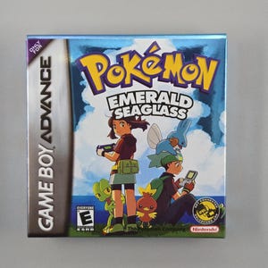 May include: A Game Boy Advance video game cartridge for Pokémon Emerald Seaglass. The box art features two characters with Pokémon, the game's title in yellow and green, and the Game Boy Advance logo.