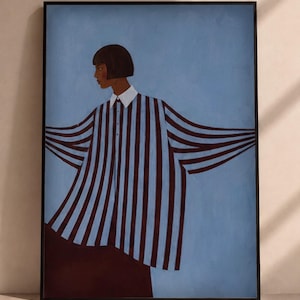 May include: A framed wall art print featuring a stylised illustration of a person with a dark bob haircut wearing a loose-fitting, long-sleeved shirt with vertical dark brown and light blue stripes and a white collar against a solid blue background.