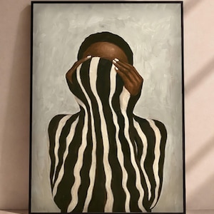 May include: A framed painting depicting a figure with dark skin wearing a black and white vertically striped garment that covers the face. The figure has hands raised to the head, and the background is a muted, light grey textured paint finish.