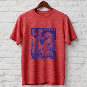 May include: Red t-shirt with a blue and red graphic of a French postage stamp. The stamp features a classical figure holding a torch, with the text "POSTES" and "REPUBLIQUE FRANCAISE".