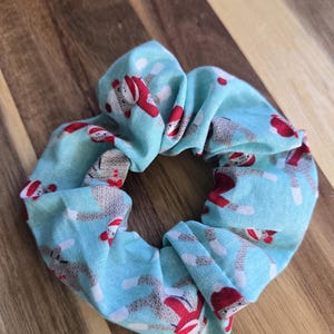 May include: A blue scrunchie with a pattern of monkeys wearing red hats. The monkeys are in a variety of poses, some are standing, some are sitting, and some are jumping. The scrunchie is made of a soft, stretchy fabric.