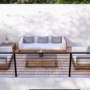K&ouml;nnte beinhalten: Gartenm&ouml;bel-Set mit einem wei&szlig;en Sofa mit drei grauen Kissen, zwei wei&szlig;en Sesseln und einem Couchtisch aus Holz. Das Set steht auf einer Holzterrasse mit schwarzen Gel&auml;ndern und Pflanzgef&auml;&szlig;en mit Gr&uuml;n.
