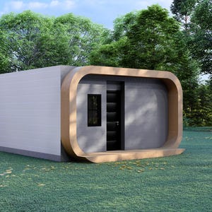 May include: A modern, minimalist cabin with a light gray exterior and a curved, wooden frame around the entrance. The cabin features a dark door and a small window, set against a backdrop of lush green trees and grass.