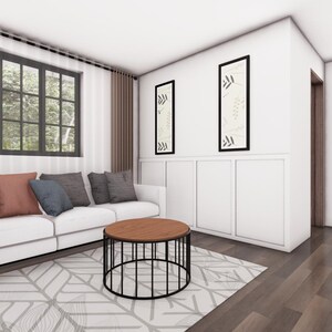 May include: A modern living room with a white sofa, colorful throw pillows, and a round coffee table. The room features a geometric patterned rug, artwork, and a window with a view of trees. The walls are white, and the floors are wood.