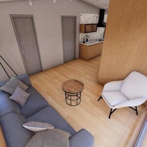 May include: Interior view of a modern living space with a blue sofa, a small round wooden table, and a white armchair. The room has light wood flooring and walls, with two closed doors and a kitchen area visible in the background. A black lamp is mounted on the wall.