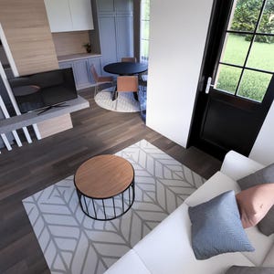 May include: An overhead view of a modern living space with a white sofa, patterned rug, and a round wooden coffee table. A black TV is mounted on a gray shelf. A black door with a window leads to a green outdoor space.
