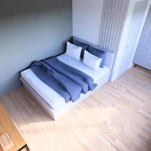 May include: A modern bedroom with a bed, desk, and wardrobe. The bed has white bedding and a blue blanket. A desk with a laptop and a chair are in the corner. The room has light wood flooring and a gray wall.