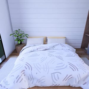 Puede incluir: Un dormitorio con una cama cubierta con un edred&oacute;n blanco con un patr&oacute;n abstracto gris. La habitaci&oacute;n tiene una ventana grande, una peque&ntilde;a planta en una mesa de madera y un armario gris. Las paredes son blancas.