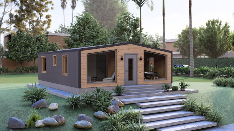 May include: A contemporary small house with a dark grey exterior and wooden features. The house has large windows, a front door, and a concrete staircase. The garden includes rocks, plants, and a green lawn.