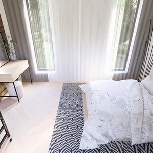 May include: A modern bedroom interior with a white bed, pillows, and a patterned blanket. A black and white patterned rug is on the floor. A white desk with a black frame and a mirror are against a brick wall.