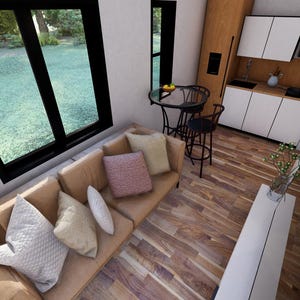 May include: Interior view of a modern living space with a tan sofa and decorative pillows. A small round table with two chairs is near a window overlooking a green lawn. The kitchen has white cabinets and a black countertop.