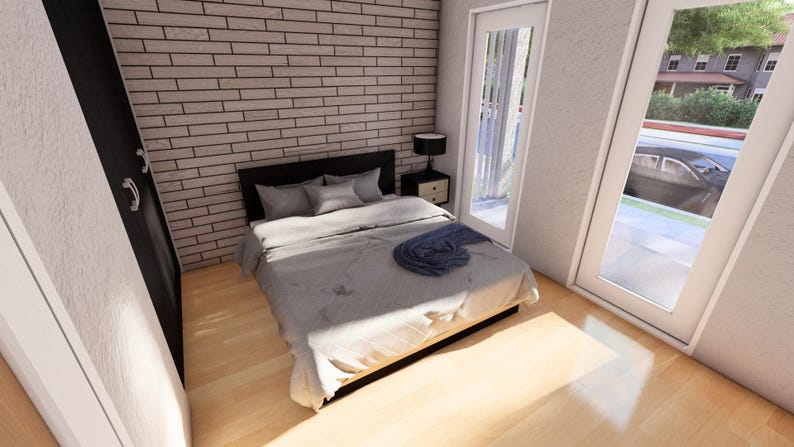 May include: A modern bedroom with a gray bedspread, pillows, and a dark headboard. A blue throw blanket rests on the bed. The room has a brick accent wall, a bedside table with a lamp, and a door leading to a balcony.