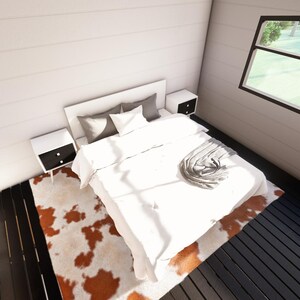 May include: A modern bedroom interior featuring a white bed with pillows and a blanket. Two white nightstands with black drawers flank the bed. A cowhide rug in shades of brown and white sits on the dark wood floor. A large window offers a view of the outdoors.