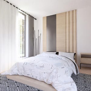 May include: A modern bedroom with a bed covered in a white and gray patterned comforter. The room features a large window with white curtains, a wooden headboard, a nightstand, and a patterned rug. The walls are painted white.