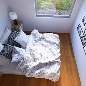 May include: An overhead view of a bedroom featuring a bed with pillows and a patterned duvet cover. A bedside table with a lamp is next to the bed. A window offers a view of greenery. Several framed pictures adorn the wall.