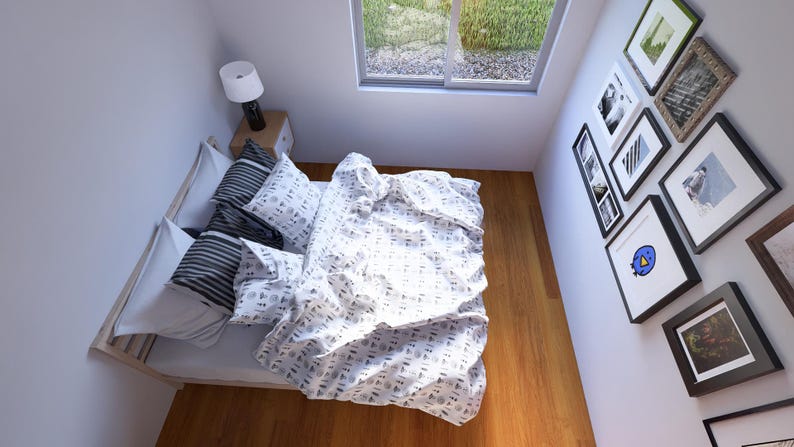 May include: An overhead view of a bedroom featuring a bed with pillows and a patterned duvet cover. A bedside table with a lamp is next to the bed. A window offers a view of greenery. Several framed pictures adorn the wall.