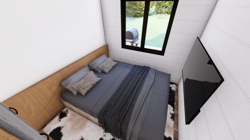 May include: A bedroom with a gray bed, pillows, and a dark gray blanket. A black TV is mounted on the wall. A window with a black frame is visible, and a cowhide rug is on the floor.