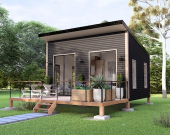 May include: A small, modern black cabin with a wooden deck and a set of patio furniture. The cabin has large windows and a flat roof. The cabin is surrounded by green grass and trees.