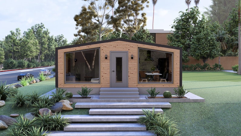 May include: A contemporary wooden house with large windows and a grey door. The house has a flat roof and is surrounded by greenery, including grass, bushes, and trees. Concrete steps lead up to the front door.