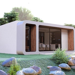 Peut inclure: Maison pr&eacute;fabriqu&eacute;e moderne et minimaliste avec un ext&eacute;rieur blanc et de grandes baies vitr&eacute;es. La maison pr&eacute;sente un design incurv&eacute; et est entour&eacute;e d'une pelouse verte, de rochers et de verdure luxuriante. L'int&eacute;rieur est visible &agrave; travers les fen&ecirc;tres.