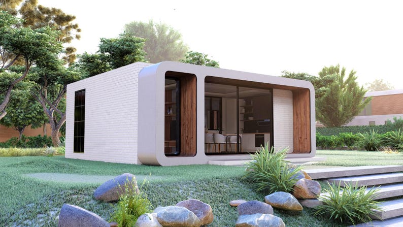 Peut inclure: Maison pr&eacute;fabriqu&eacute;e moderne et minimaliste avec un ext&eacute;rieur blanc et de grandes baies vitr&eacute;es. La maison pr&eacute;sente un design incurv&eacute; et est entour&eacute;e d'une pelouse verte, de rochers et de verdure luxuriante. L'int&eacute;rieur est visible &agrave; travers les fen&ecirc;tres.