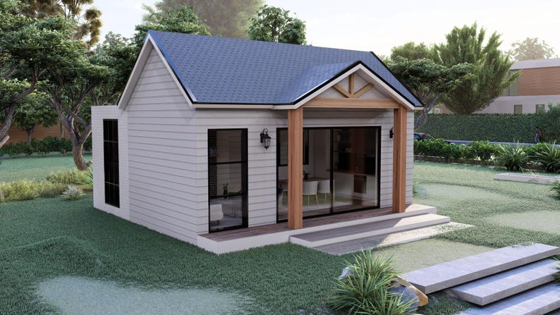 Puede incluir: Una peque&ntilde;a casa de color gris claro con un tejado azul y ventanas y puertas con marcos negros. La casa tiene un porche con vigas de madera y est&aacute; rodeada de hierba verde y &aacute;rboles. Unas escaleras de hormig&oacute;n conducen al porche.