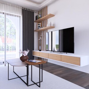 May include: Modern living room with a large flat-screen TV mounted on a white wall. The room features a white sofa, a light-colored rug, and a coffee table. The room has a large window with sheer curtains and dark gray drapes.