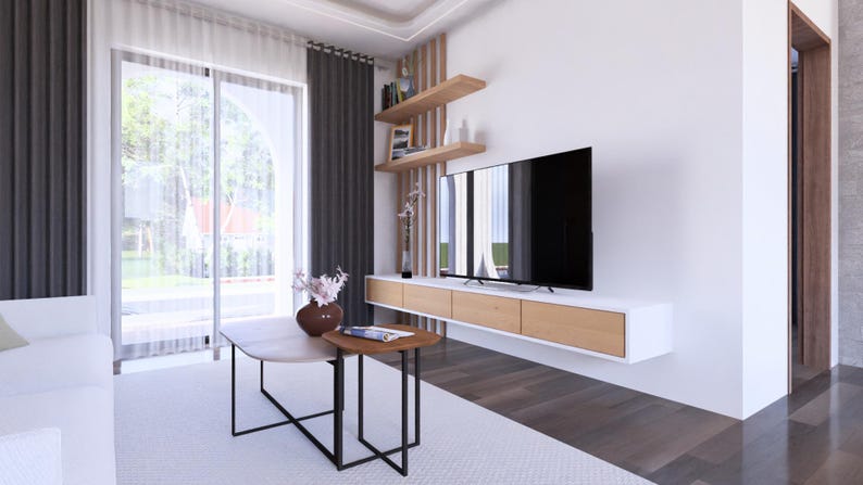 May include: Modern living room with a large flat-screen TV mounted on a white wall. The room features a white sofa, a light-colored rug, and a coffee table. The room has a large window with sheer curtains and dark gray drapes.