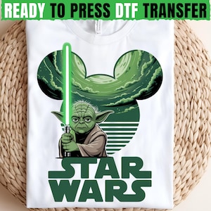 May include: White t-shirt with a green Yoda graphic holding a green lightsaber. The design includes a green Mickey Mouse head shape and the words "STAR WARS" in green. The text "READY TO PRESS DTF TRANSFER" is at the top.