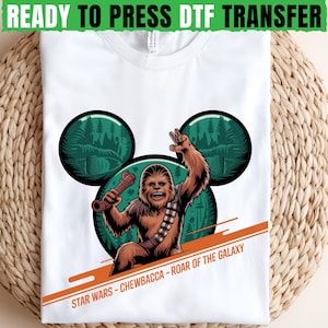 May include: White t-shirt featuring a Chewbacca graphic with a forest scene in the background. The design includes the text "STAR WARS - CHEWBACCA - ROAR OF THE GALAXY" and "READY TO PRESS DTF TRANSFER". The Chewbacca character is holding a weapon.