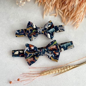May include: Two bow ties with a dark blue background and a colorful animal print. The bow ties are made of fabric and have a classic bow tie shape.