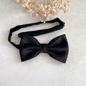 May include: A black bow tie with a satin finish. The bow tie is on a white background.