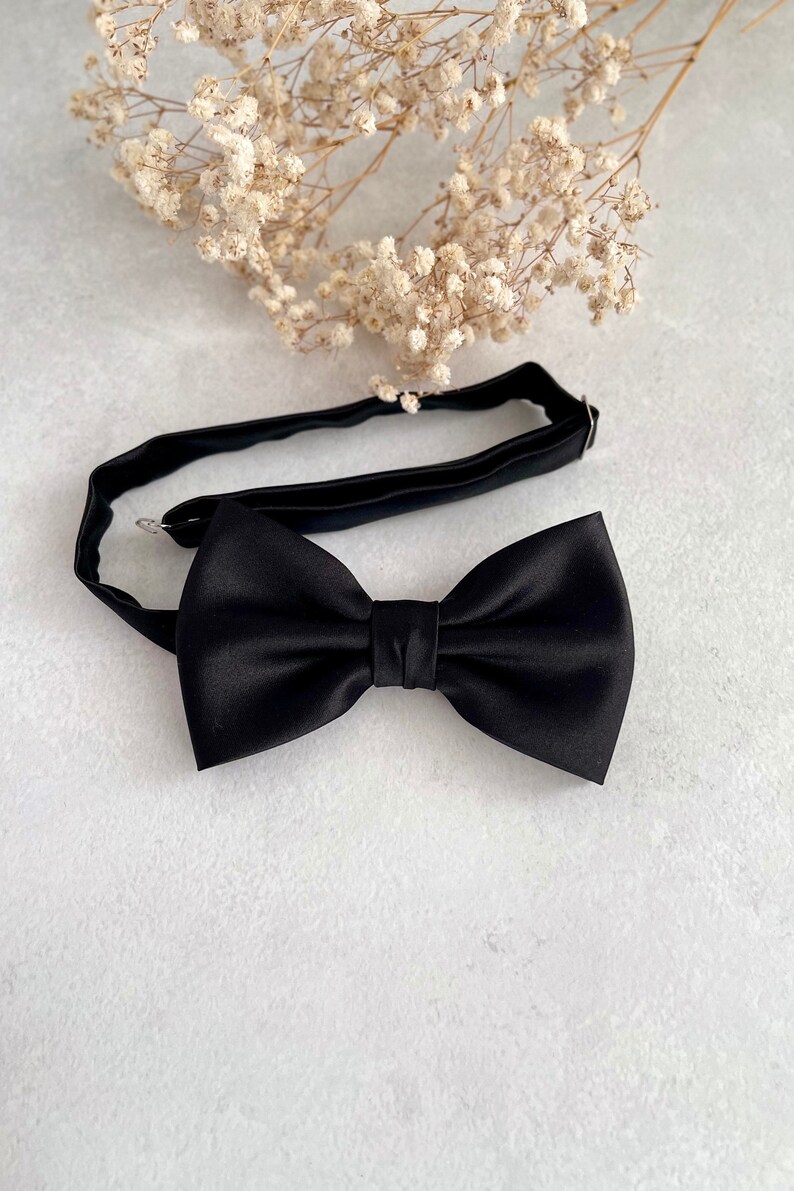 May include: A black bow tie with a satin finish. The bow tie is on a white background.