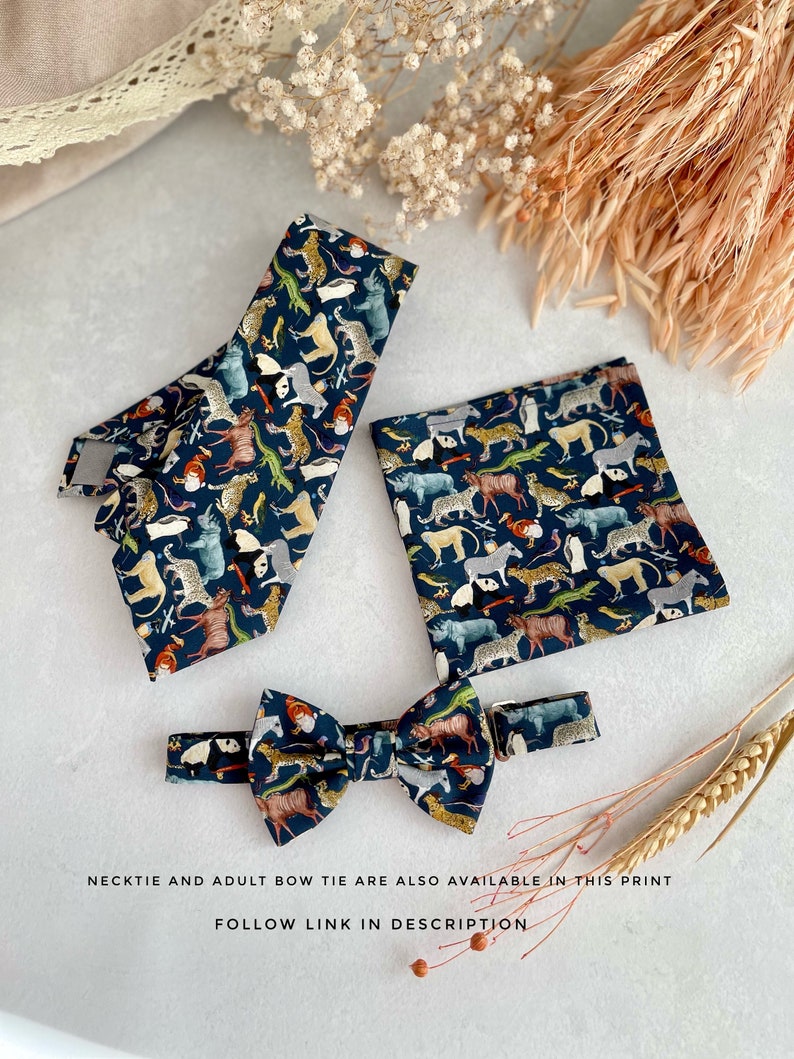 May include: A set of three bow ties featuring a dark blue background with a colorful animal print. The set includes a standard bow tie, a smaller bow tie, and a pocket square.