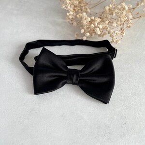 May include: A black satin bow tie with a classic design. The bow tie is tied and ready to wear.