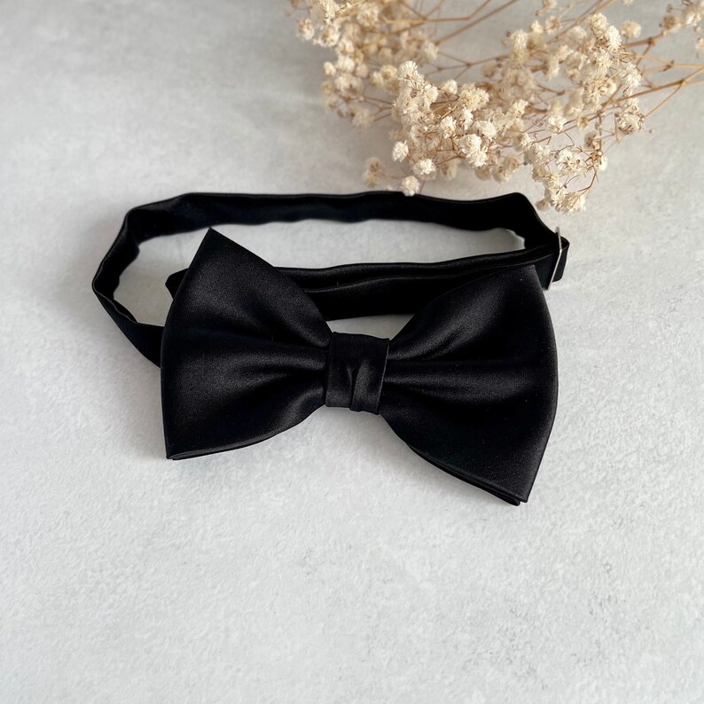 May include: A black satin bow tie with a classic design. The bow tie is tied and ready to wear.