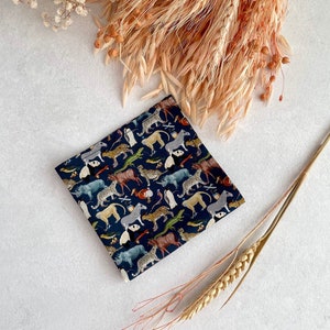 May include: A dark blue fabric square with a repeating pattern of various animals, including zebras, leopards, and rhinoceroses. The fabric is surrounded by dried wheat stalks and white flowers.