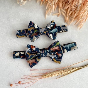 May include: Two bow ties with a dark blue background and a colorful animal print. The bow ties are made of fabric and have a classic bow tie shape.