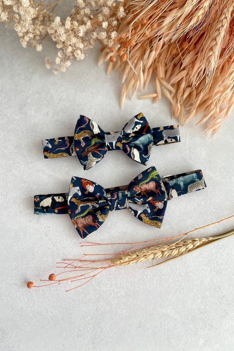 May include: Two bow ties with a dark blue background and a colorful animal print. The bow ties are made of fabric and have a classic bow tie shape.
