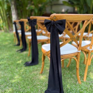 May include: Wooden chairs with black fabric bows tied on the back. The chairs are arranged in a row on a green lawn.