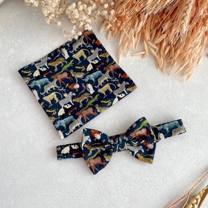 May include: A dark blue bow tie and pocket square with a colorful animal print pattern. The pattern includes animals like zebras, leopards, and pandas.