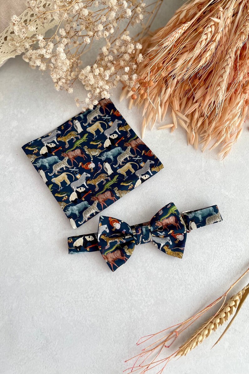May include: A dark blue bow tie and pocket square with a colorful animal print pattern. The pattern includes animals like zebras, leopards, and pandas.