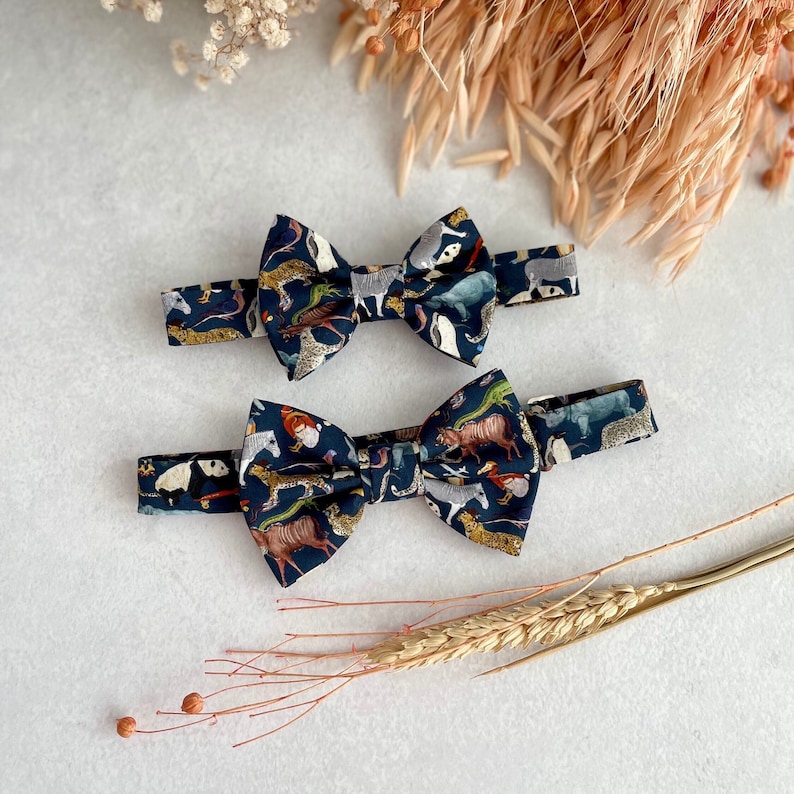 May include: Two bow ties with a dark blue background and a colorful animal print. The bow ties are made of fabric and have a classic bow tie shape.