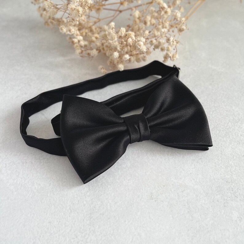 May include: A black satin bow tie with a classic design. The bow tie is tied and ready to wear.